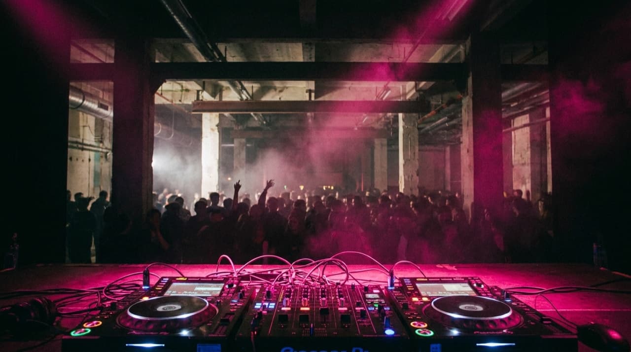 A dark venue crowd silhouetted in neon pink haze